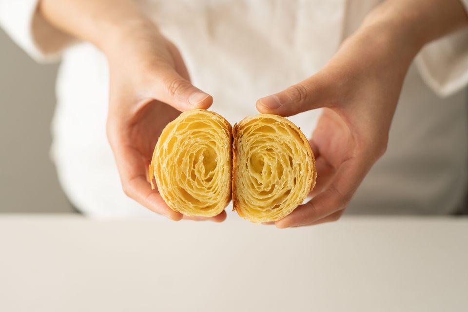 Two hands holding a freshly baked croissant split in half, revealing its laminated, honeycomb-like interior.