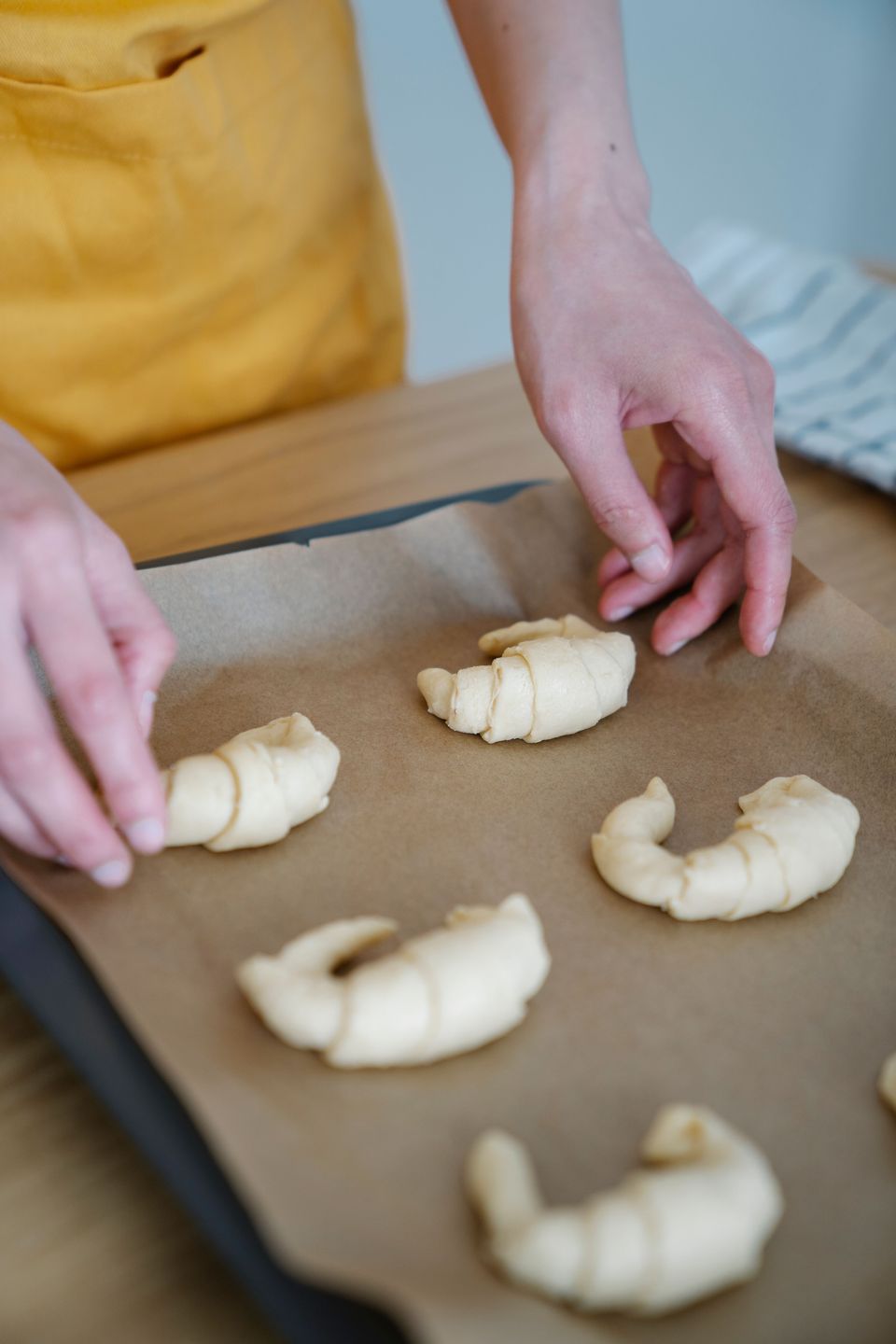 Hands arranging shaped, unbaked croissants onto a parchment-lined tray, ready for proofing and baking.