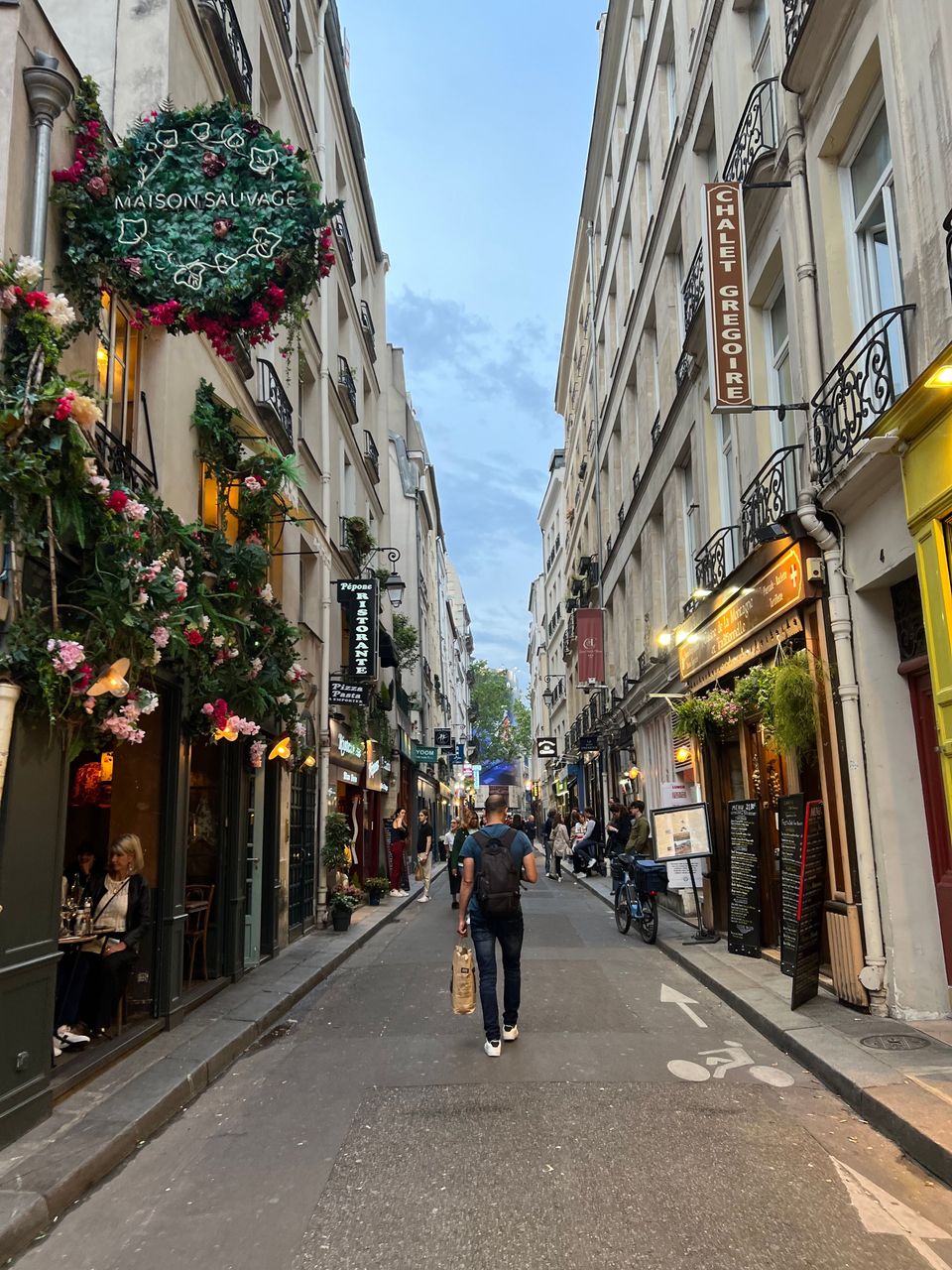 Pedestrians walking along a narrow Paris street lined with caf&eacute;s and restaurants